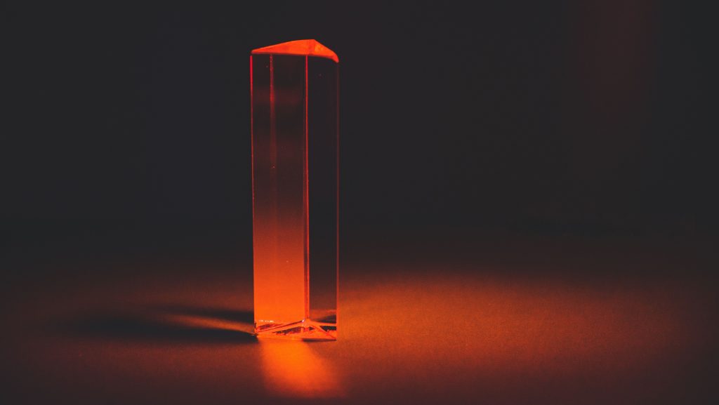 A translucent glass prism glowing under a warm red light against a dark background.